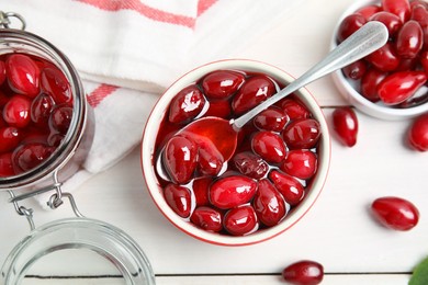 Photo of Delicious dogwood jam with berries on white wooden table, flat lay