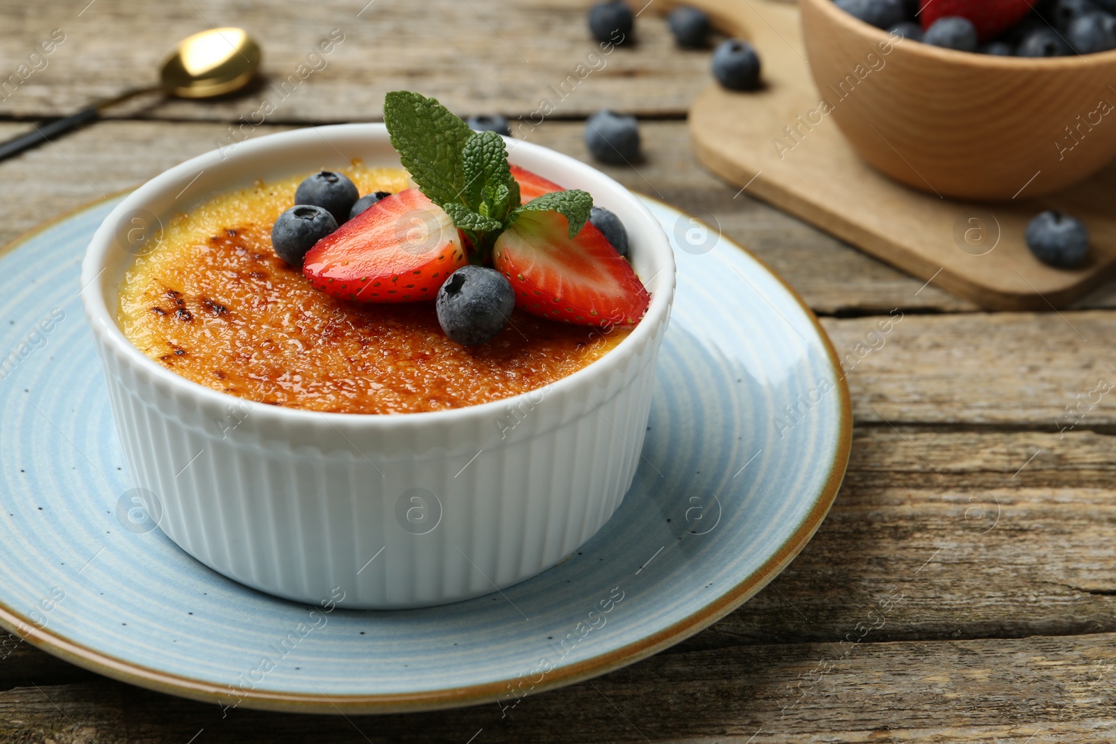 Photo of Delicious creme brulee with berries and mint in bowl on wooden table, closeup