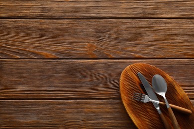 Photo of New board and cutlery on wooden table, top view with space for text