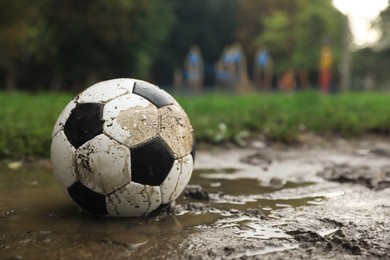 Dirty leather soccer ball in puddle outdoors, space for text