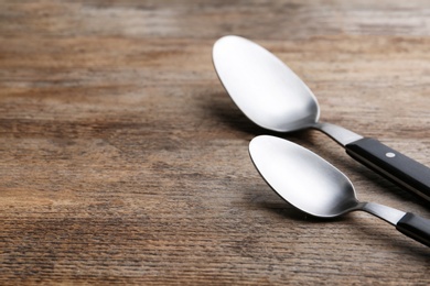 Clean empty table spoons on wooden background, space for text