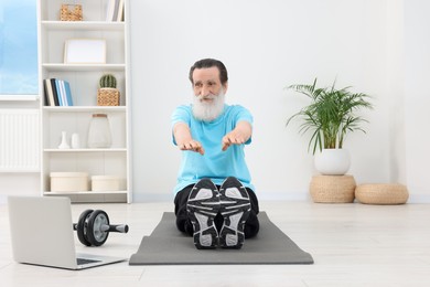 Photo of Senior man in sportswear stretching while watching online tutorial at home