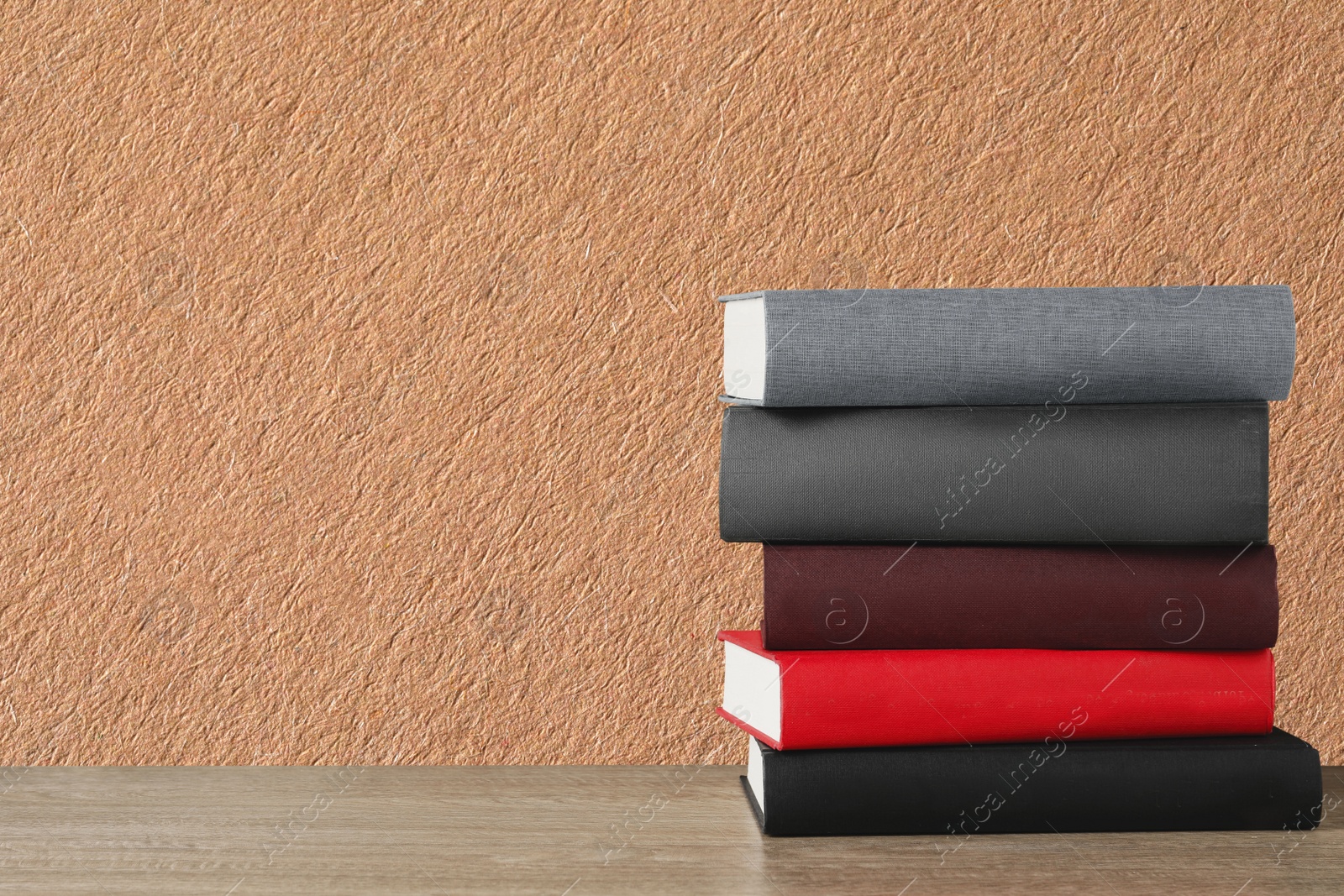 Image of Many stacked hardcover books on wooden table against beige textured background, space for text