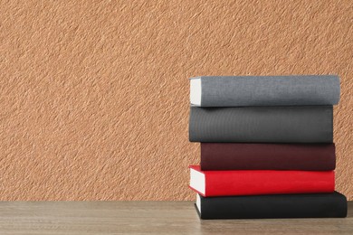 Many stacked hardcover books on wooden table against beige textured background, space for text