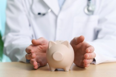 Photo of Doctor with piggy bank at wooden table, closeup