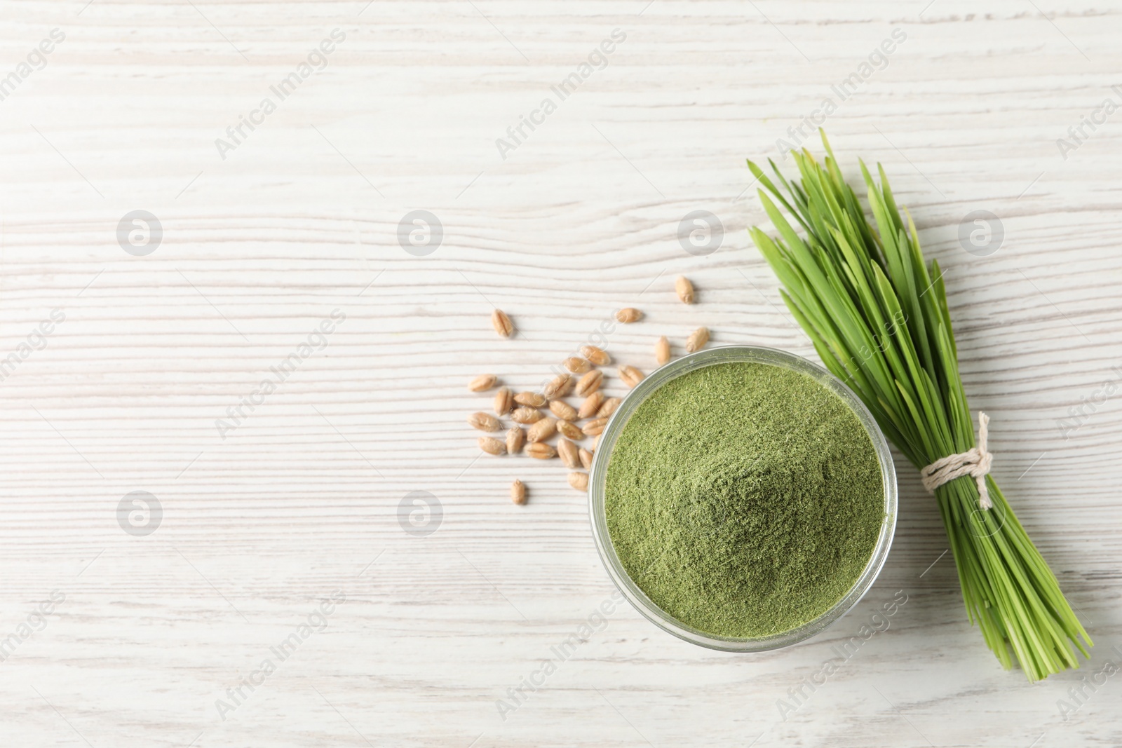 Photo of Wheat grass powder in bowl, seeds and fresh sprouts on white wooden table, flat lay. Space for text