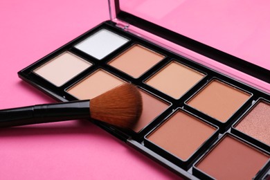 Photo of Colorful contouring palette with brush on pink background, closeup. Professional cosmetic product
