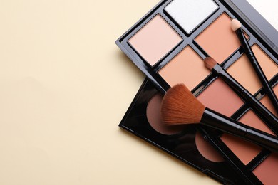 Photo of Colorful contouring palettes with brushes on beige background, flat lay. Space for text