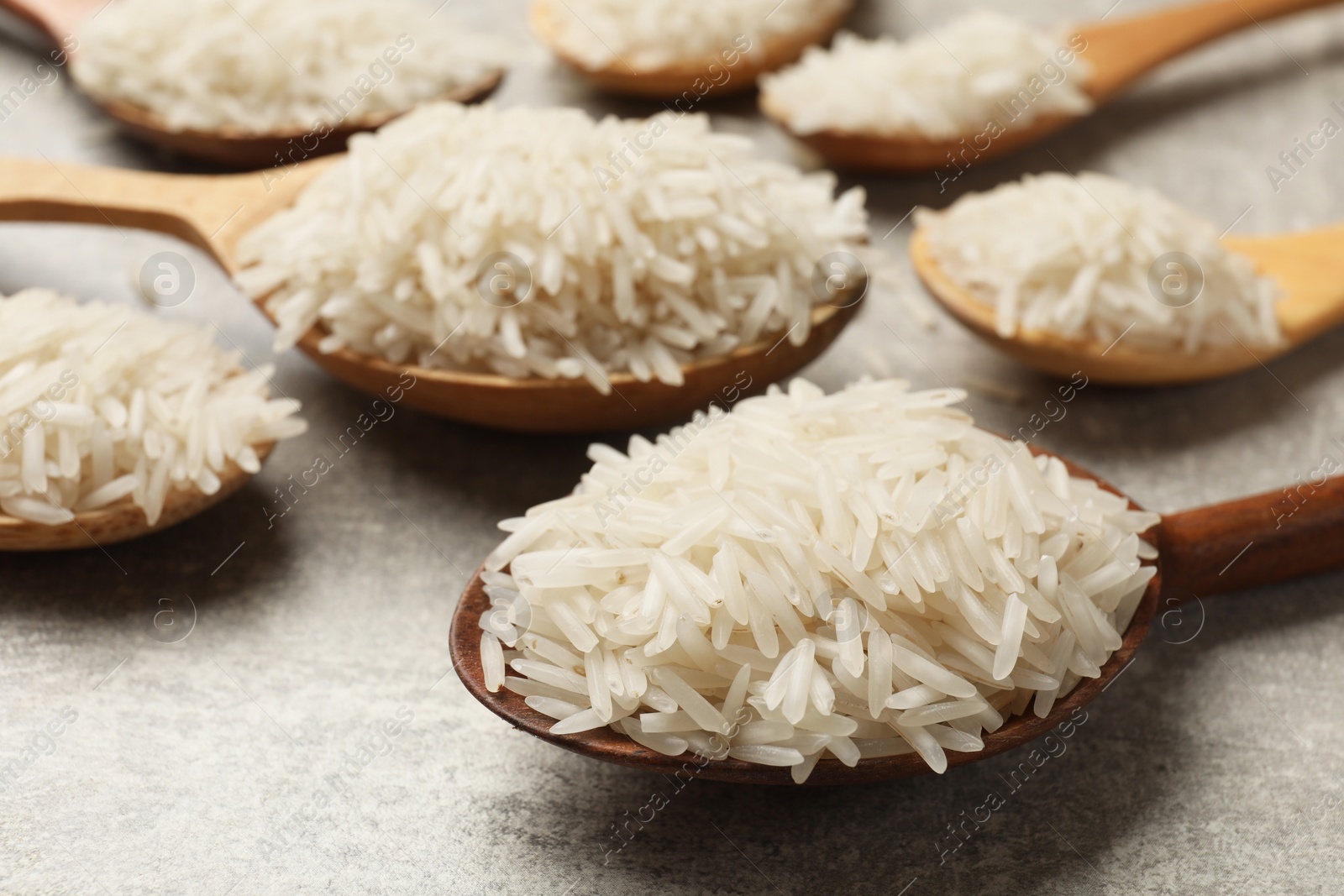 Photo of Raw basmati rice in spoons on grey table, closeup