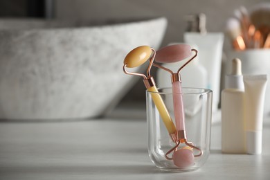 Photo of Natural face rollers and cosmetic products on counter in bathroom. Space for text