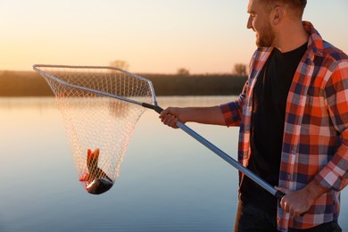 Fisherman holding fishing net with catch at riverside, closeup