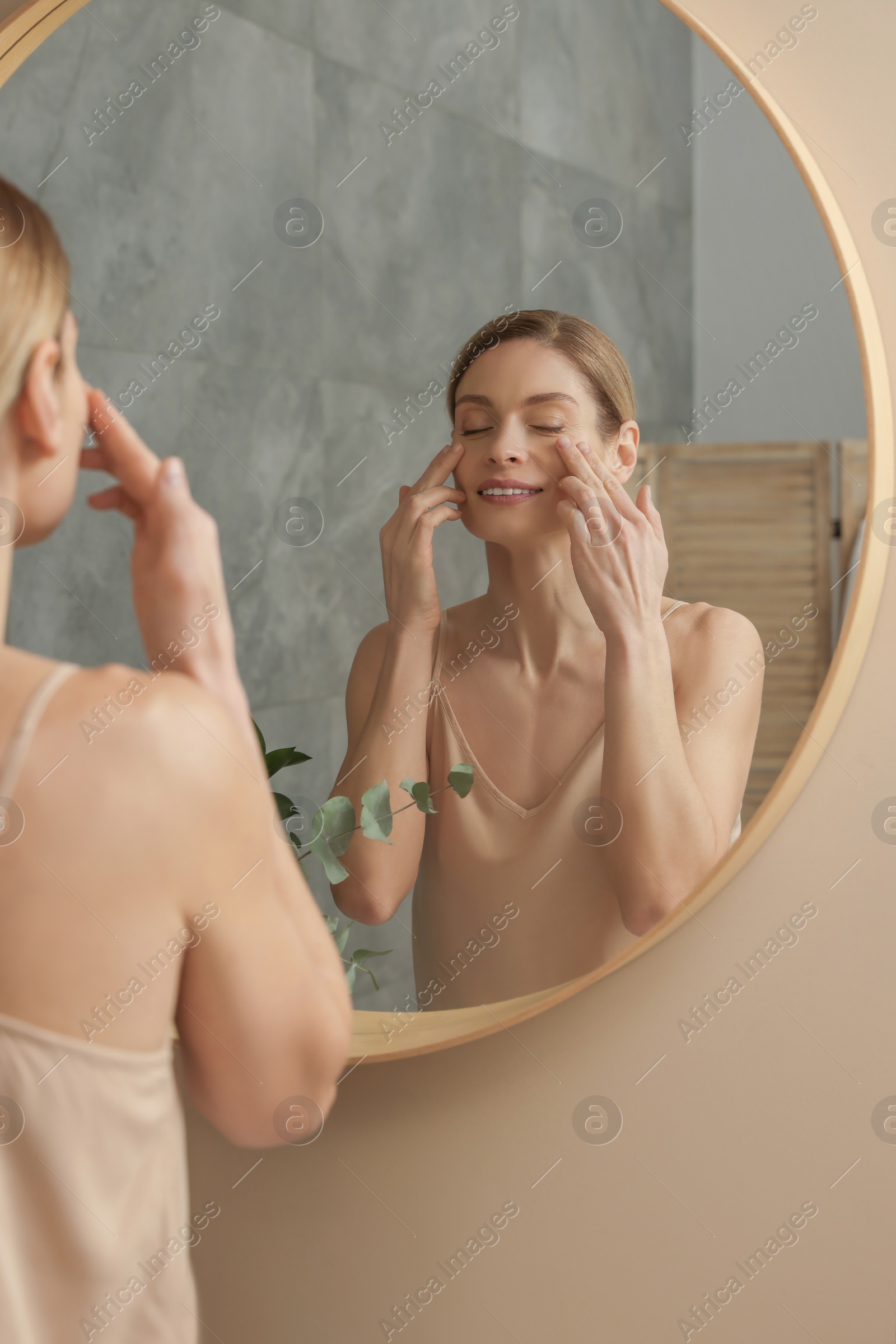 Photo of Woman massaging her face near mirror in bathroom