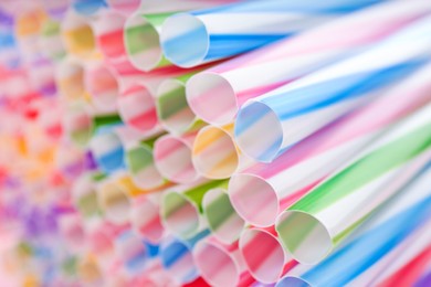 Photo of Heap of colorful plastic straws for drinks as background, closeup