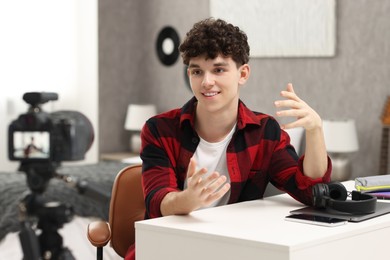 Photo of Smiling teenage blogger explaining something while streaming at home