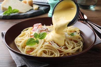 Photo of Pouring tasty cheese sauce onto spaghetti with meat on wooden table, closeup