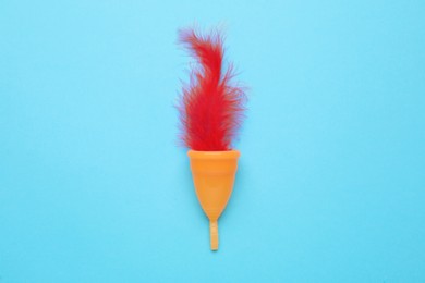 Photo of Menstrual cup with red feather on light blue background, top view
