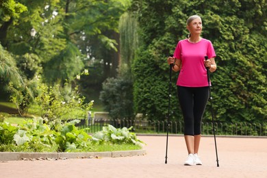 Senior woman performing Nordic walking outdoors, space for text. Low angle view