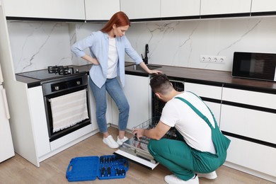 Photo of Woman looking how serviceman repairing her dishwasher in kitchen