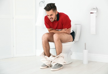 Photo of Young man suffering from diarrhea on toilet bowl at home