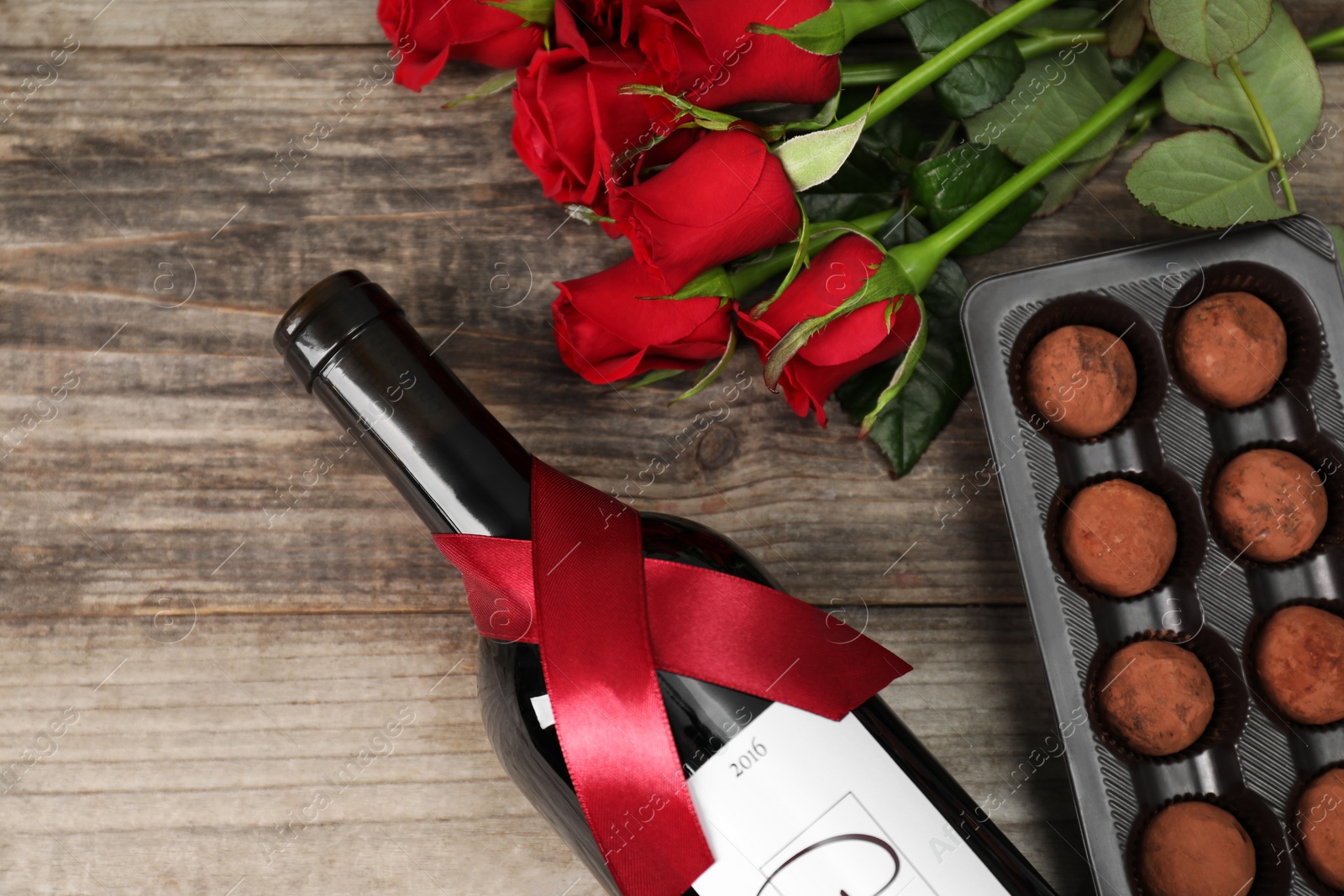 Photo of Bottle of red wine, chocolate truffles and roses on wooden table, flat lay. Space for text