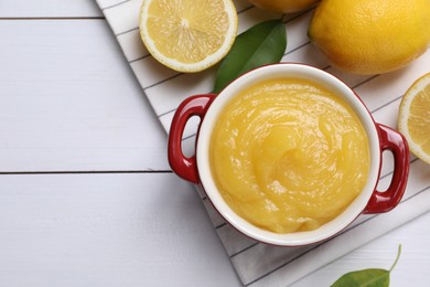 Photo of Delicious lemon curd in bowl and fresh citrus fruits on white wooden table, flat lay. Space for text
