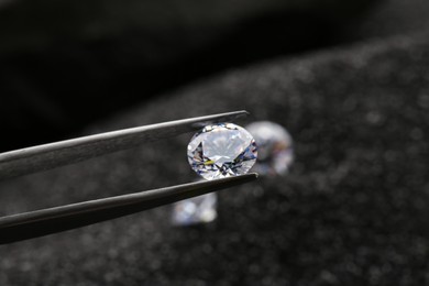 Tweezers with beautiful shiny diamond on dark background, closeup