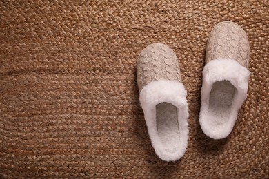 Pair of warm stylish slippers on wicker carpet, top view. Space for text