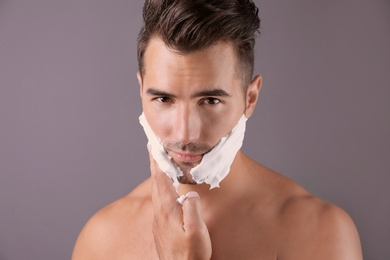 Handsome young man applying shaving foam on color background