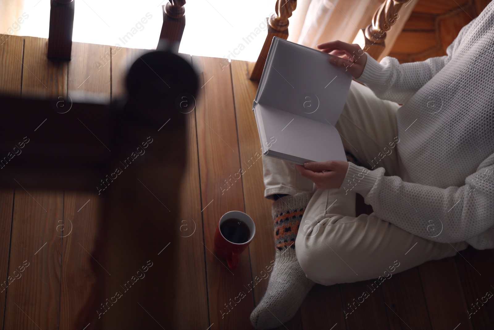 Photo of Woman with cup of coffee reading book at home, closeup