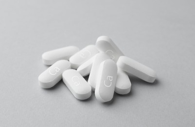 Photo of Pile of calcium supplement pills on light grey background, closeup