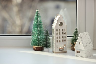 Photo of Beautiful house shaped candle holders and small fir trees on windowsill indoors, space for text