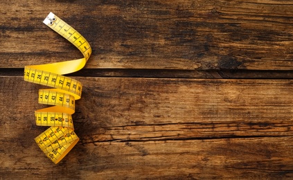 Yellow measuring tape on wooden table, top view. Space for text