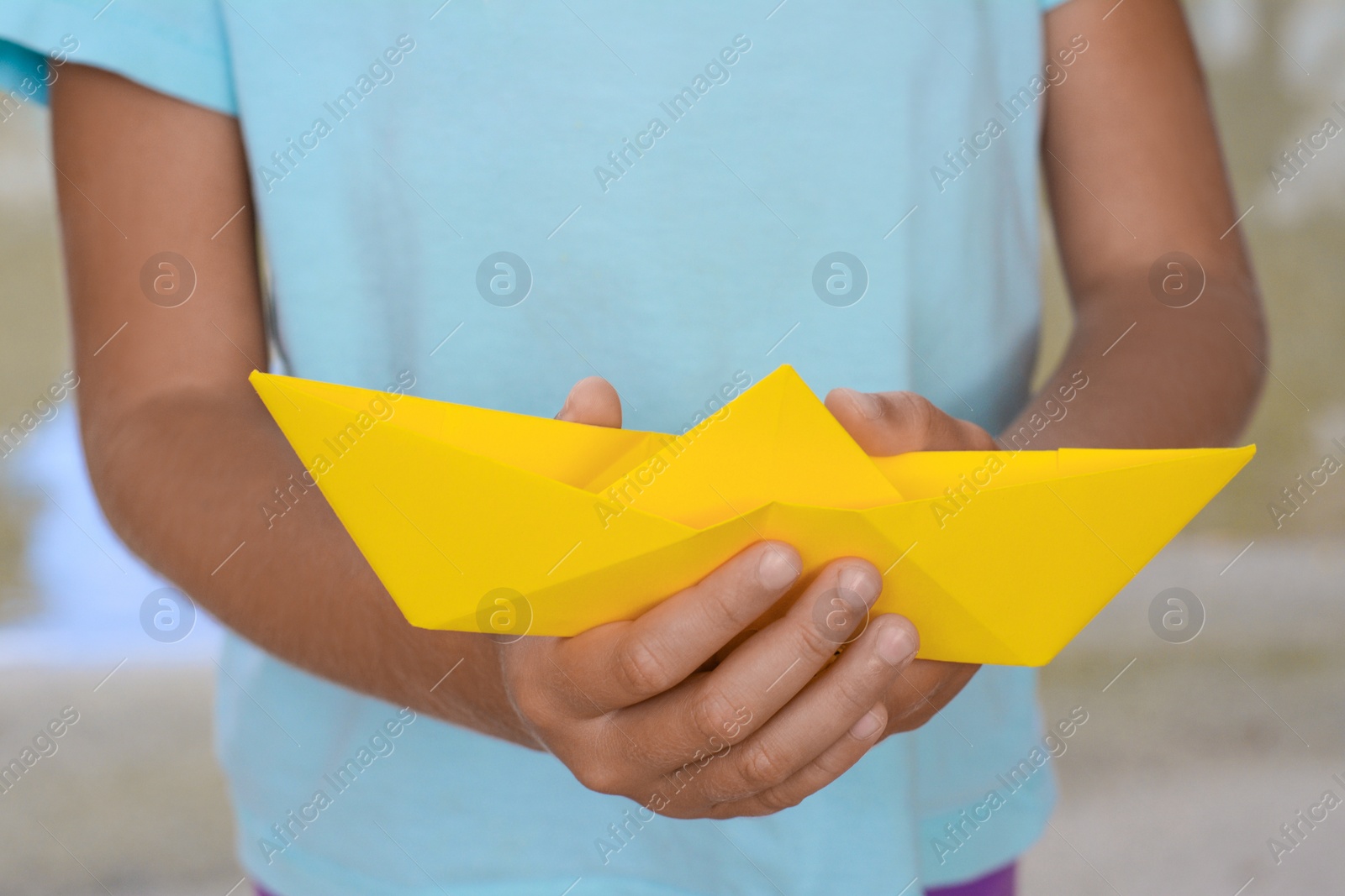 Photo of Little girl holding yellow paper boat outdoors, closeup