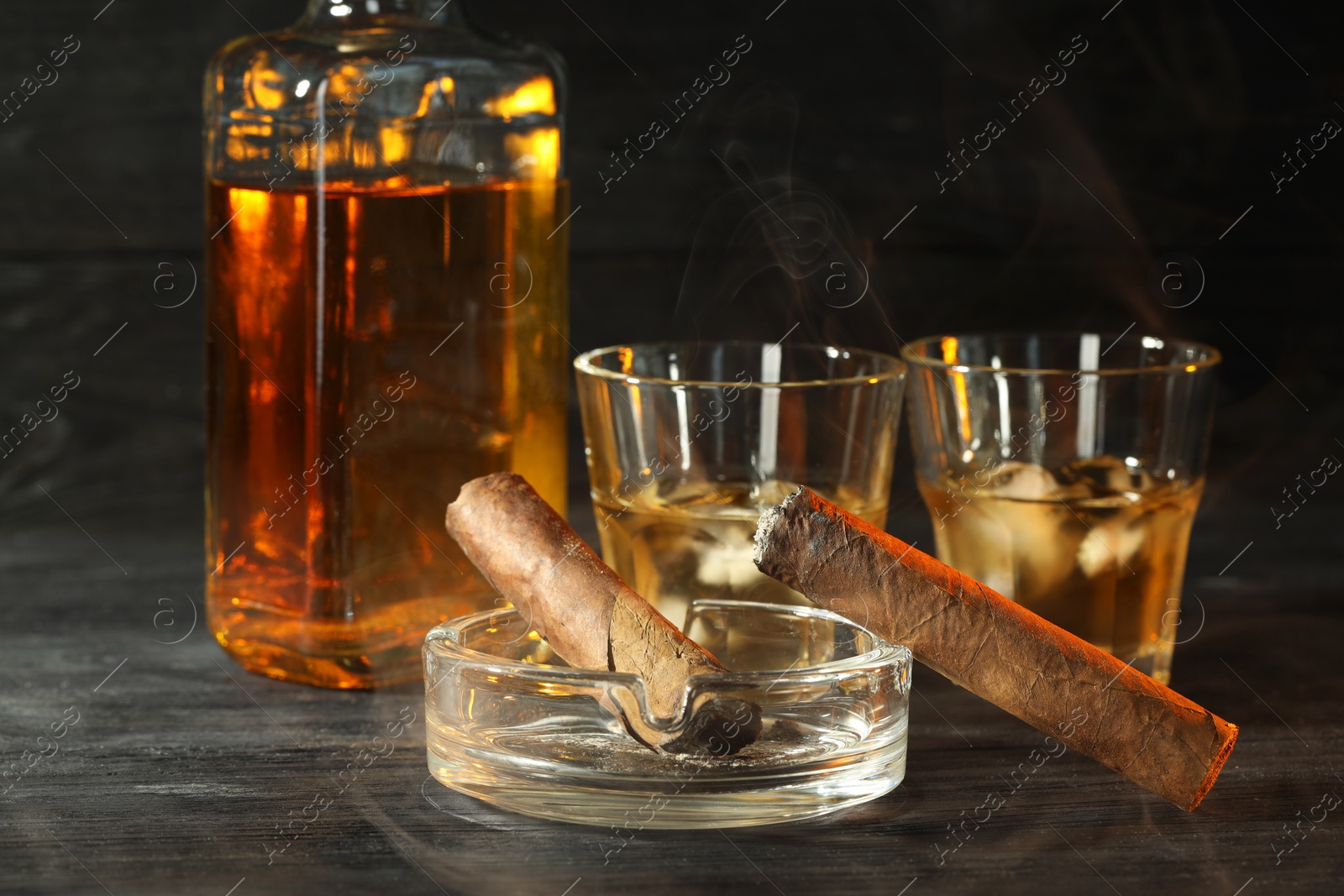 Photo of Cigars, ashtray and whiskey with ice cubes on black wooden table