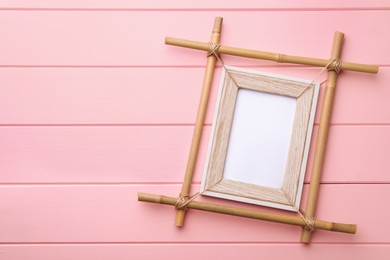 Photo of Empty bamboo frame on pink wooden background, top view. Space for text