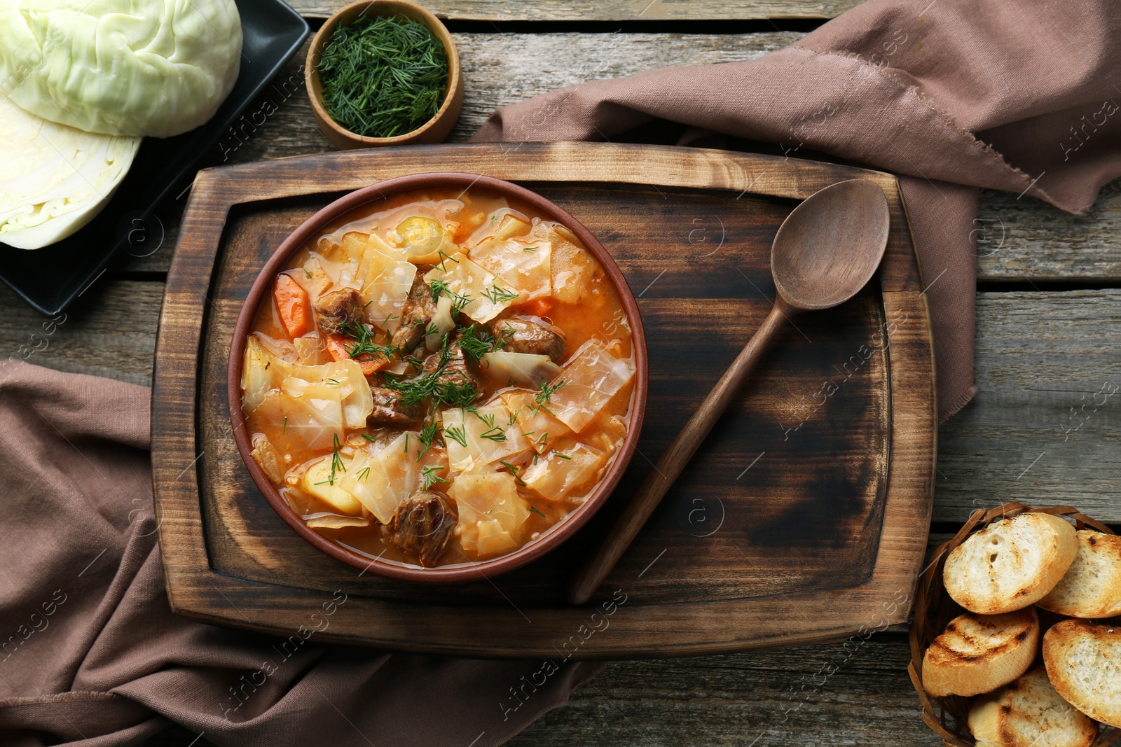 Photo of Tasty cabbage soup with meat, carrot and ingredients on wooden table, flat lay