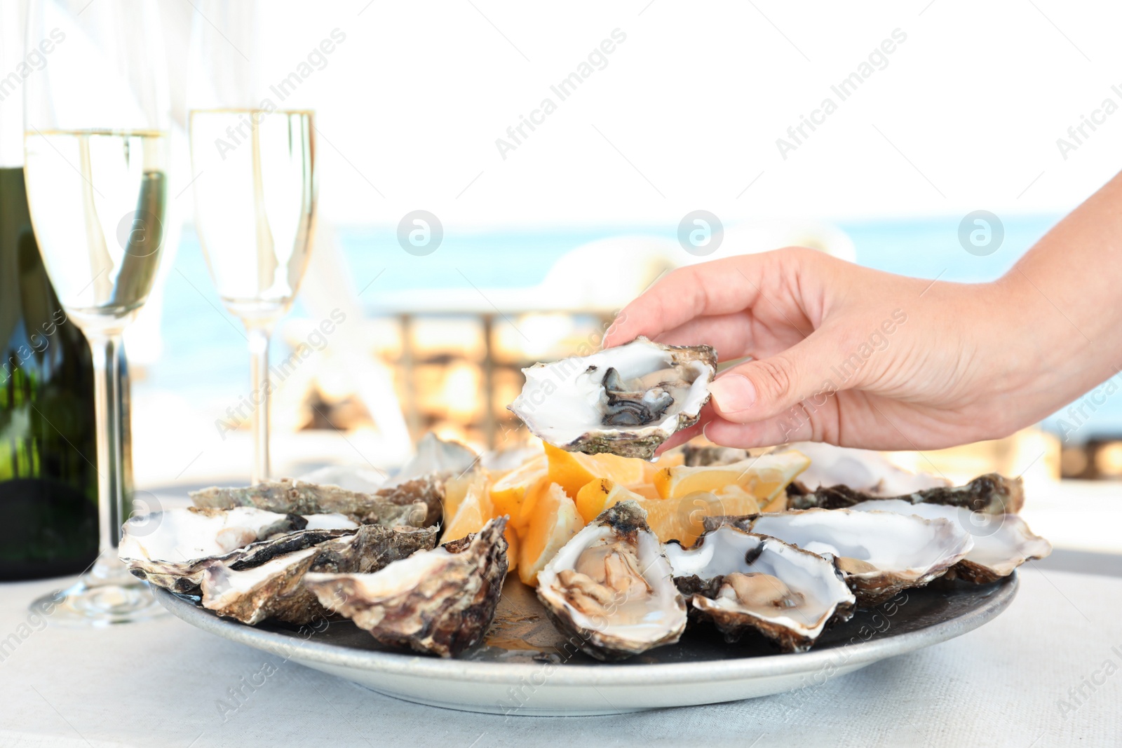 Photo of Woman holding fresh oyster over plate, focus on hand