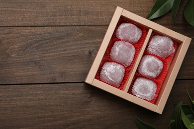 Box of delicious mochi and leaves on wooden table, flat lay with space for text. Traditional Japanese dessert