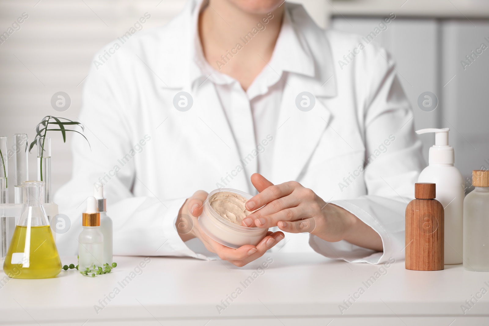 Photo of Dermatologist with jar testing cosmetic product at white table indoors, selective focus