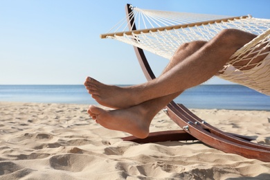 Photo of Young man relaxing in hammock on beach, closeup
