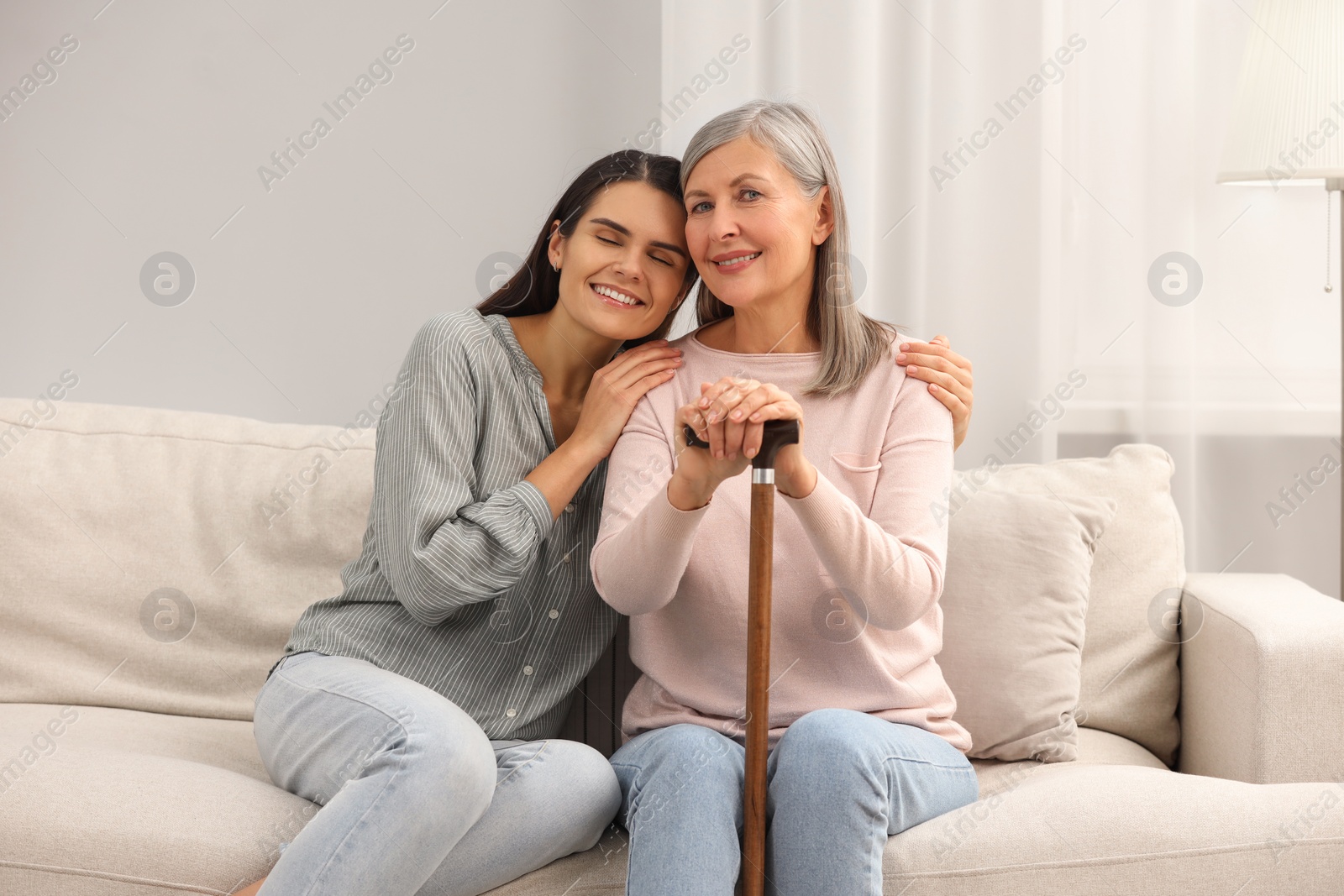 Photo of Mature lady with walking cane and young woman on sofa at home