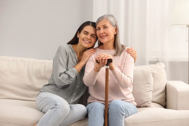 Mature lady with walking cane and young woman on sofa at home