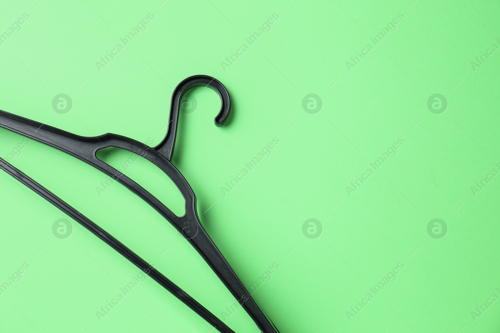 Photo of Empty black hanger on light green background, top view. Space for text