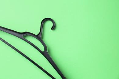 Empty black hanger on light green background, top view. Space for text