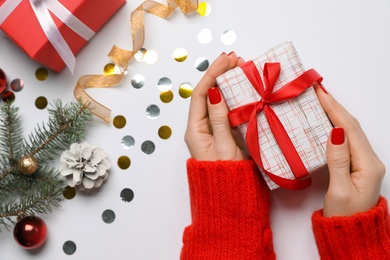 Photo of Woman holding gift box near fir tree branch with Christmas decor on white background, top view