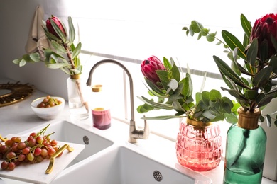 Photo of Vases with beautiful protea flowers near sink in kitchen. Interior design