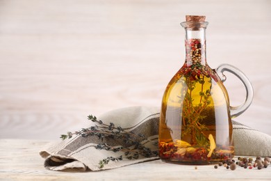 Photo of Glass jug of cooking oil with spices and herbs on white wooden table. Space for text