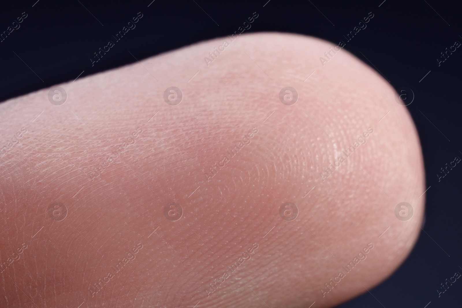 Photo of Finger with friction ridges on dark background, macro view