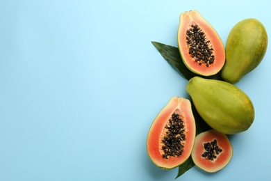 Photo of Fresh ripe papaya fruits with green leaves on light blue background, flat lay. Space for text