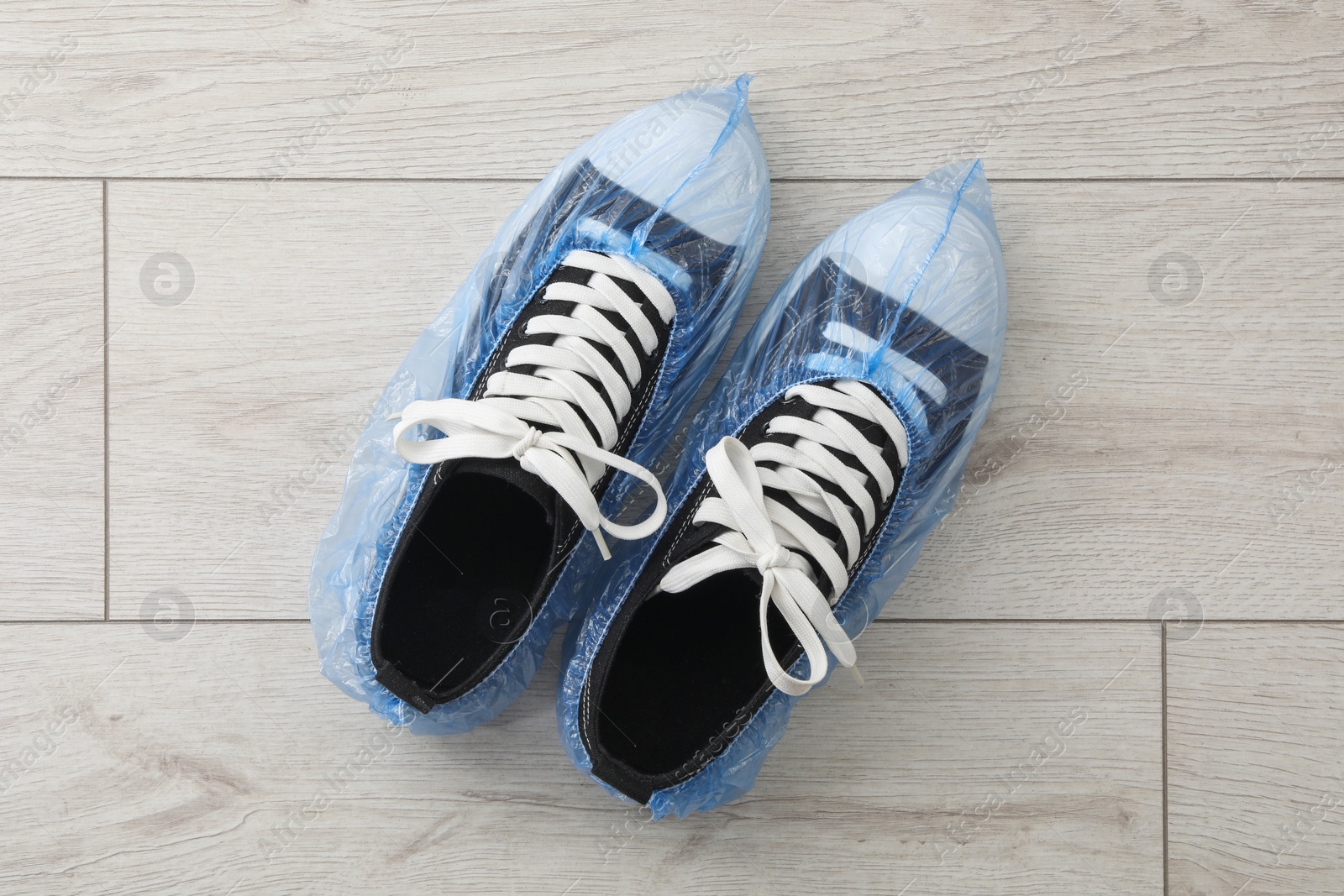 Photo of Sneakers in blue shoe covers on light wooden floor, top view